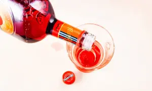 Czerwony Martini Fiero drink nalewany z butelki do szklanki. Obok leży czerwona zakrętka.