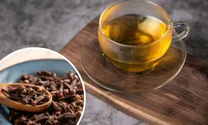 Aromatyczna woda z goździkami w szklanej filiżance, obok miseczka pełna goździków na drewnianej desce.
