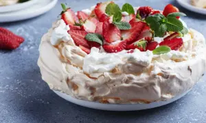 Puszysty tort bezowy z mascarpone i bitą śmietaną, ozdobiony świeżymi truskawkami i miętą.