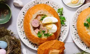 Pyszny żur w chlebie z kiełbasą i jajkiem, ozdobiony natką pietruszki. Na stole wielkanocne dekoracje: pisanki w gnieździe, zajączek.