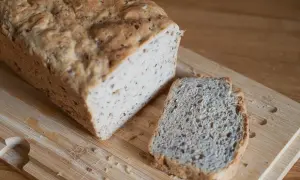 Chleb z siemienia lnianego, z jedną kromką obok, na drewnianej desce. Idealny na zdrowe śniadanie.