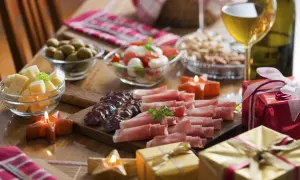 Pyszne menu na sylwestra w domu: deska wędlin i serów, oliwki, pomidorki z mozzarellą, orzechy, wino i prezenty.