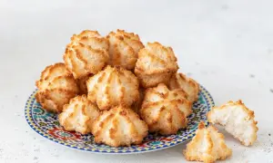 Stare przepisy na kokosanki to skarb! Na talerzu z marokańskim wzorem ułożono stosik puszystych, złotych ciasteczek kokosowych.