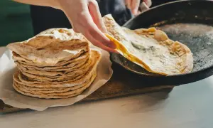 Stos świeżo upieczonego lawaszu obok patelni, na której właśnie smaży się kolejny. Pyszne, cienkie placki gotowe do podania.