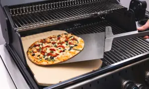 Pyszne ciasto na grilla z kurczakiem, suszonymi pomidorami i oliwkami jest wsuwane na kamień do pizzy.