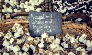 Kuszek nugatu z czekoladą i migdałami. Tabliczka informuje: "Nugat mit Schoko und Mandeln 100g 2€".