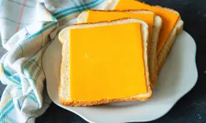 Gotowe do zrobienia pyszne tosty z airfryer. Trzy kromki chleba z serem cheddar na białym talerzyku.