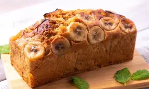 Pyszny chlebek bananowy Ani gotuje się w piekarniku. Z wierzchu ozdobiony plasterkami banana i listkami mięty.