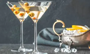 Dwa kieliszki martini z oliwkami, obok srebrna miseczka z lodem i cytryną. Idealne do podania z czym pić martini.