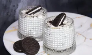 Dwa deserki z kremem i pokruszonymi oreo ciastkami, ozdobione połówkami ciastek.