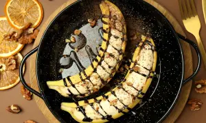 Szybki deser z bananów: połówki bananów zapieczone z orzechami, polane czekoladą i posypane kakao.