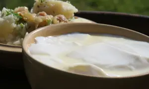 Gęste, białe zsiadłe mleko w glinianej miseczce, obok ziemniaków z koperkiem. Prosty przepis, jak zrobić zsiadłe mleko.
