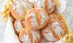 Koszyk pełen świeżych, puszystych bułek ziemniaczanych, posypanych mąką. Idealne na śniadanie lub jako dodatek do obiadu.