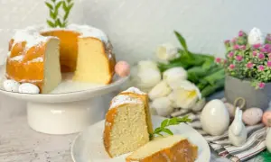 Puszysta babka z białek, oprószona cukrem pudrem, na wielkanocnym stole z tulipanami i pisankami.