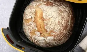 Chleb z airfryer, rumiany i lekko oprószony mąką, czeka na wyjęcie.