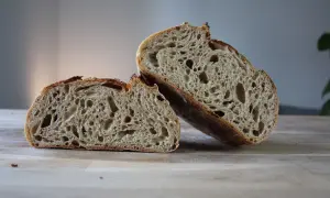 Chleb pszenno żytni na zakwasie, przekrojony na pół, ukazuje puszysty miąższ z licznymi dziurami i chrupiącą skórkę.