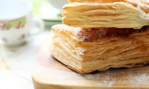 Stos warstw ciasta francuskiego, idealny do nauki, jak zrobić ciasto francuskie. Posypane cukrem pudrem, na drewnianej desce.