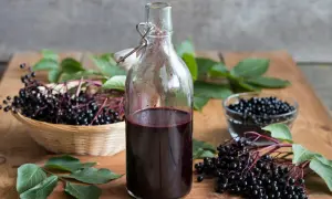 Sok z czarnego bzu – przepis babci. Świeże owoce i gotowy, ciemny sok w butelce na drewnianym blacie.