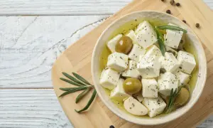 Kostki sera feta w oliwie z oliwkami, czosnkiem i rozmarynem, na desce.