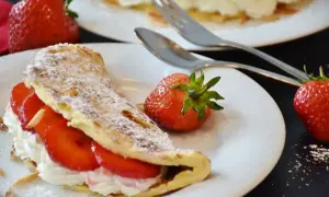 Pyszny omlet z białek z bitą śmietaną i truskawkami, posypany cukrem pudrem i płatkami migdałów. Idealny deser.