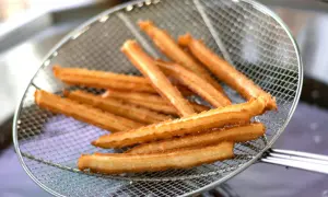 Złociste churros na sicie, właśnie wyjęte z gorącego oleju. Pytasz churros co to? To pyszny, smażony przysmak!