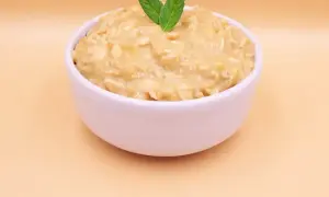 Pyszna owsianka z bananem, udekorowana listkami mięty, w białej miseczce na jasnym tle.