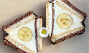 Dwa kawałki ciasta z sera z wiaderka, przypominające chatkę Puchatka, z bananem w środku i ozdobione stokrotką.