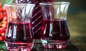 Dwa kieliszki wypełnione rubinową nalewką z czeremchy, obok butelka i kiść owoców.