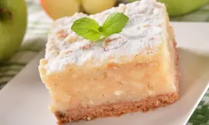 Pyszny kawałek ekspresowego ciasta z jabłkami, posypany cukrem pudrem i udekorowany listkiem mięty.