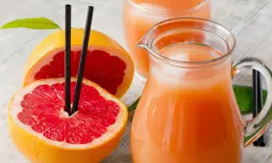 Orzeźwiający sok z grejpfruta w dzbanku i szklance, obok przekrojonych owoców. Idealny na upalne dni.