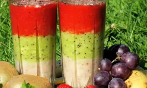Warstwowy koktajl owocowy z truskawkami, kiwi i bananem, ozdobiony startą czekoladą. Obok owoce: winogrona, kiwi, truskawki, banan.