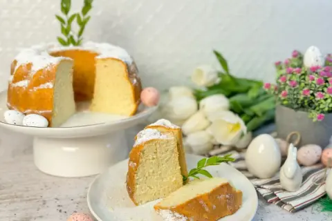 Puszysta babka z białek, oprószona cukrem pudrem, na wielkanocnym stole z tulipanami i pisankami.