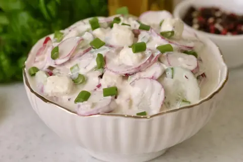 Rewelacyjna sałatka na grilla z rzodkiewką, ogórkiem i serem feta w kremowym sosie, posypana szczypiorkiem. Idealna na letnie przyjęcia.