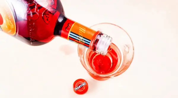 Czerwony Martini Fiero drink nalewany z butelki do szklanki. Obok leży czerwona zakrętka.