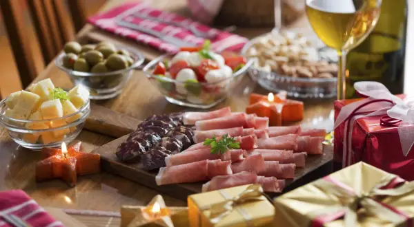 Pyszne menu na sylwestra w domu: deska wędlin i serów, oliwki, pomidorki z mozzarellą, orzechy, wino i prezenty.