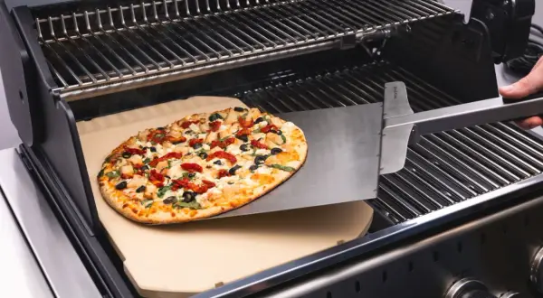 Pyszne ciasto na grilla z kurczakiem, suszonymi pomidorami i oliwkami jest wsuwane na kamień do pizzy.