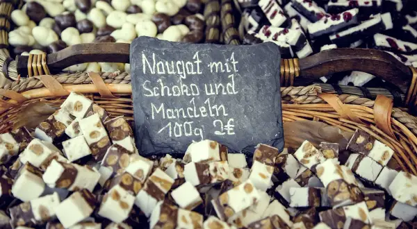 Kuszek nugatu z czekoladą i migdałami. Tabliczka informuje: "Nugat mit Schoko und Mandeln 100g 2€".