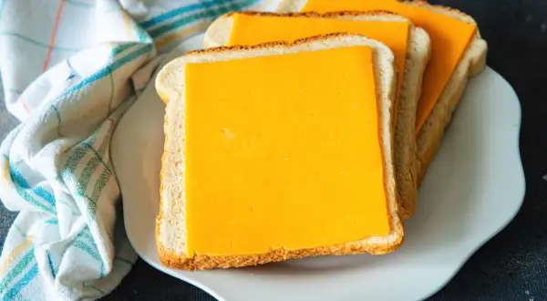 Gotowe do zrobienia pyszne tosty z airfryer. Trzy kromki chleba z serem cheddar na białym talerzyku.
