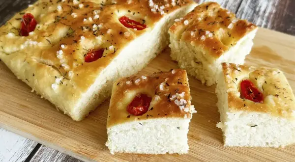 Puszysta, oryginalna włoska focaccia przepis z pomidorkami i solą morską, pokrojona na kawałki, gotowa do degustacji.