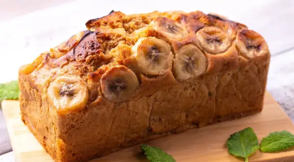 Pyszny chlebek bananowy Ani gotuje się w piekarniku. Z wierzchu ozdobiony plasterkami banana i listkami mięty.