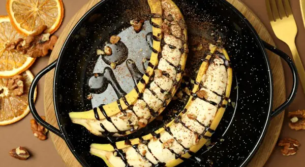 Szybki deser z bananów: połówki bananów zapieczone z orzechami, polane czekoladą i posypane kakao.