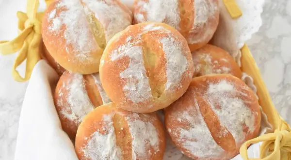 Koszyk pełen świeżych, puszystych bułek ziemniaczanych, posypanych mąką. Idealne na śniadanie lub jako dodatek do obiadu.