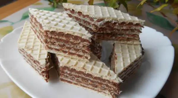 Trójkątne wafle przełożone kremem z mleka w proszku, ułożone na białym talerzu.