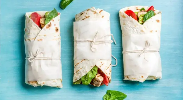 Trzy tortille zawinięte w papier, z widocznym nadzieniem z kurczaka, pomidorów i szpinaku. Idealne na keto tortilla przepis.