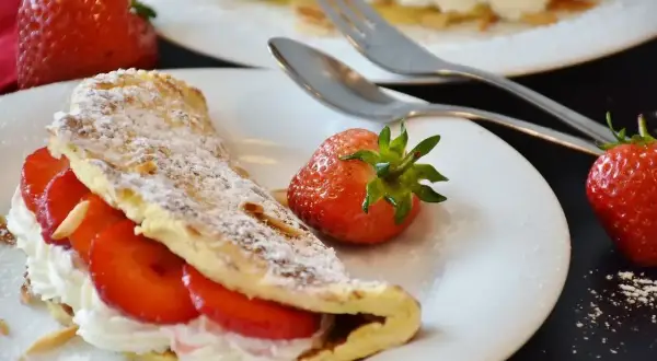 Pyszny omlet z białek z bitą śmietaną i truskawkami, posypany cukrem pudrem i płatkami migdałów. Idealny deser.