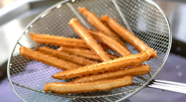 Złociste churros na sicie, właśnie wyjęte z gorącego oleju. Pytasz churros co to? To pyszny, smażony przysmak!