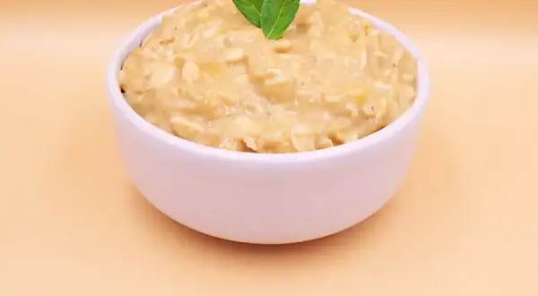 Pyszna owsianka z bananem, udekorowana listkami mięty, w białej miseczce na jasnym tle.