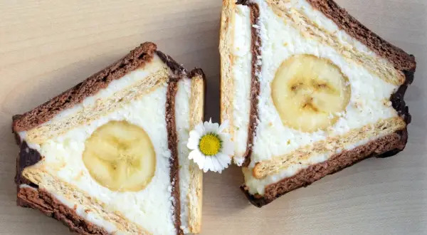 Dwa kawałki ciasta z sera z wiaderka, przypominające chatkę Puchatka, z bananem w środku i ozdobione stokrotką.