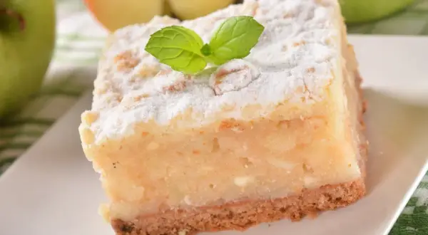 Pyszny kawałek ekspresowego ciasta z jabłkami, posypany cukrem pudrem i udekorowany listkiem mięty.