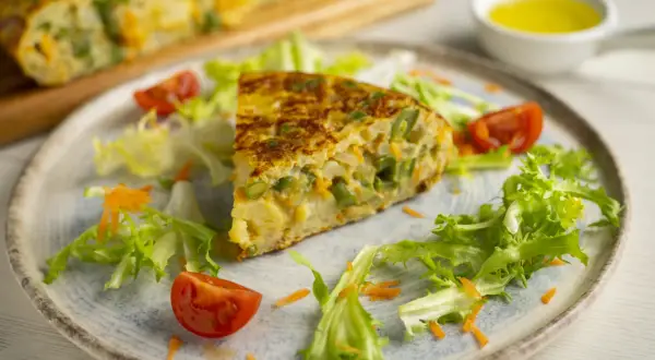 Pyszny omlet z piekarnika z fasolką szparagową i marchewką, podany z sałatką i pomidorkami.
